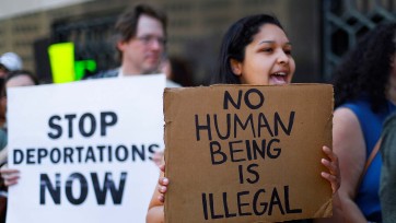 Person holds sign that reads No Human Being is Illegal